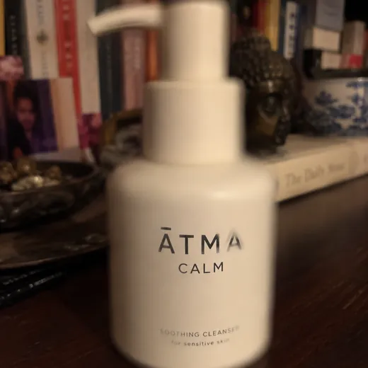 Phone snap of a bottle in portrait mode, the whole frame soft, a busy bookshelf behind it in dim light