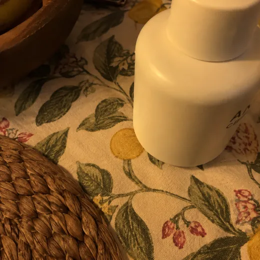 Phone snap of a bottle on a patterned tablecloth, tilted, the top cut off by the edge of the frame, warm lamp light