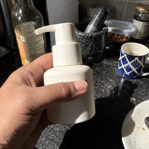 Phone snap of a bottle held in a hand, fingers over the label, cluttered kitchen behind it and a hard shadow